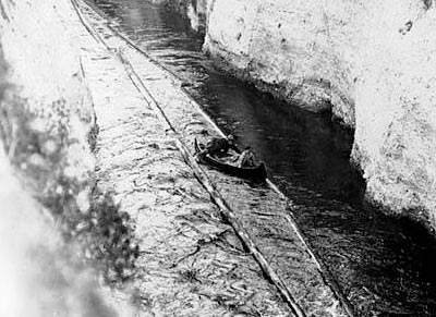 Looking west at canoeists traveling through the Montlake Ditch in 1904. The canoe is within the log chute created by two log shear booms that guided logs through the ditch to Lake Union. Courtesy UW Special Collections, UW22317z